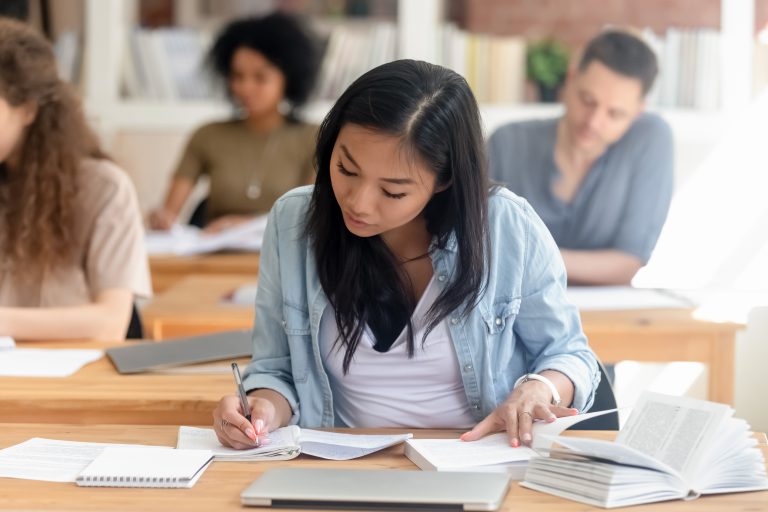 A JC Economics student focuses on writing notes during her first tuition lesson, practising essay frameworks and data response analysis under the guidance of a tutor.