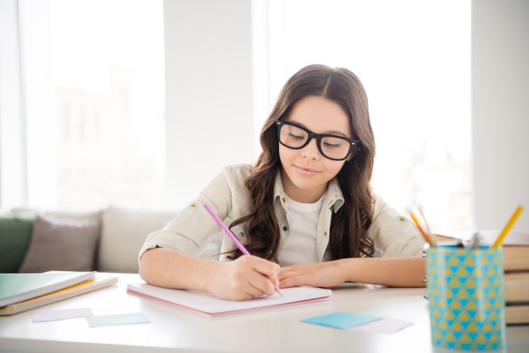 Student writing notes at a bright desk, focused on JC Economics exam preparation and effective study practice.